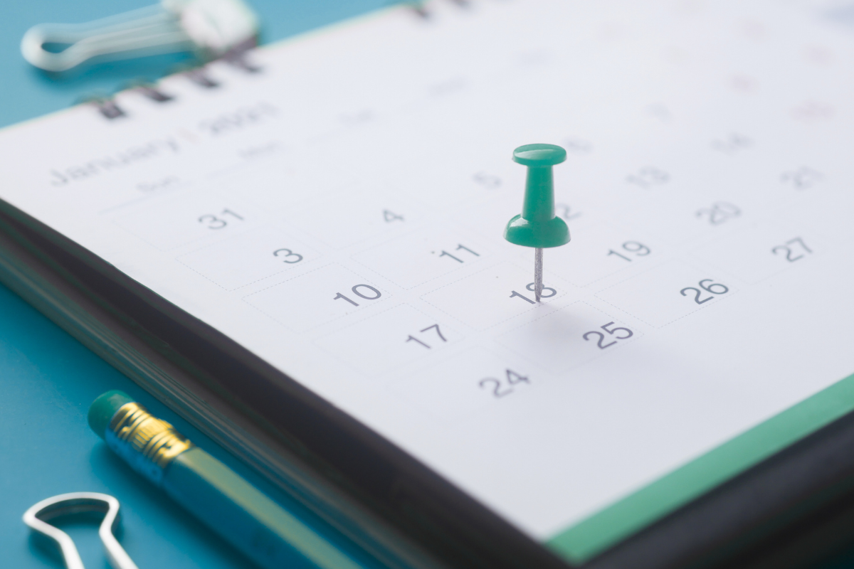 A green pin stuck into a paper calendar